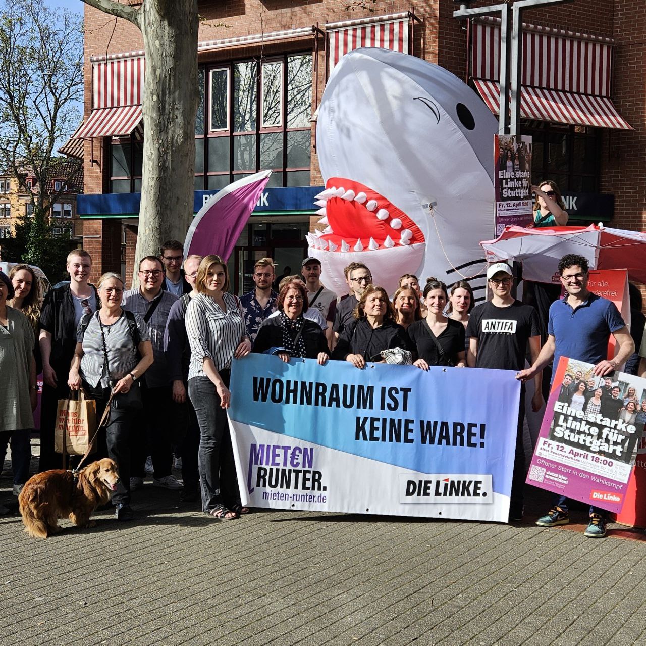 Teilnehmer:innen der Kundgebung Mieten Runter halten ein Banner auf dem steht: Wohnraum ist keine Ware. Im Hintergrund ist ein großer Aufblasbarer Hai.